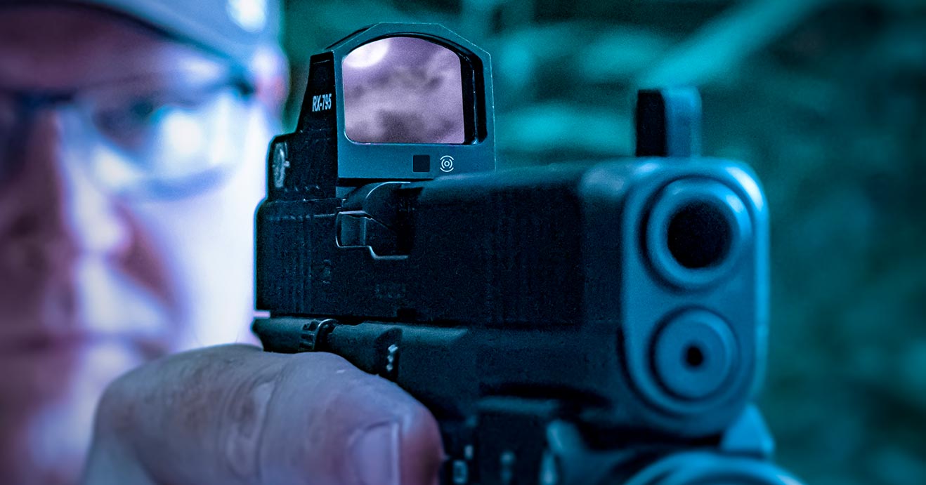 man holding a pistol with a cuda red dot sight at night